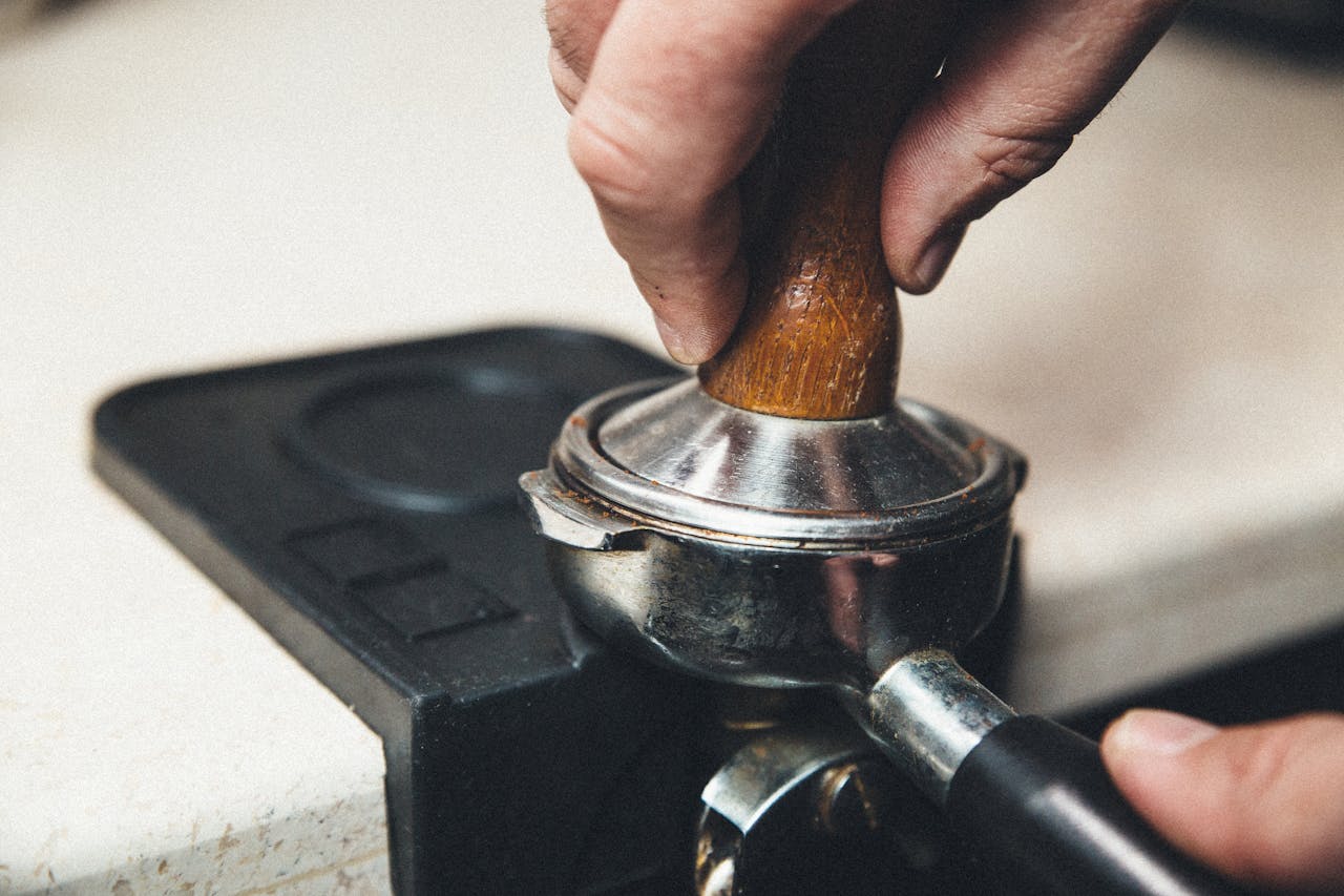 Detailed view of a barista using a tamper on a portafilter for espresso preparation.